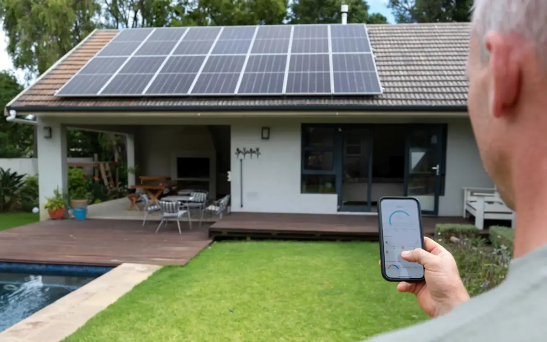 Zu sehen ist ein Mann von hinten der sein Handy in der Hand hat und Richtung seiner PV-Anlage am Dach schaut.