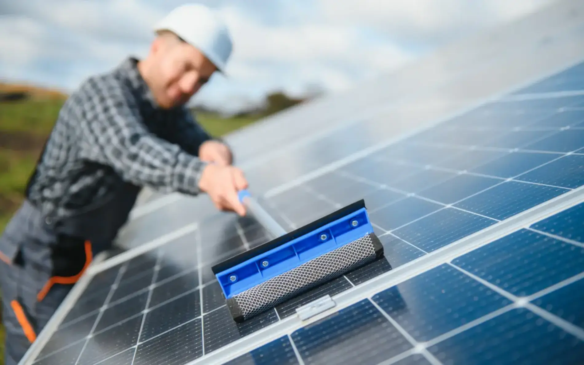 Zu sehen ist ein Arbeiter mit Helm der eine PV anlage abwischt