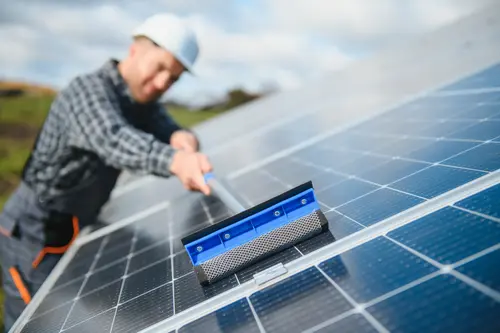 Zu sehen ist ein Arbeiter mit Helm der eine PV anlage abwischt