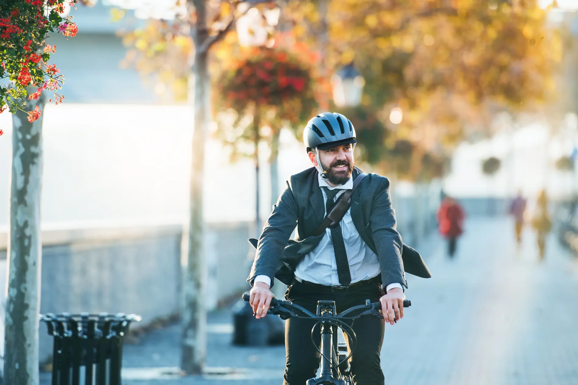 Mann mit Helm und Sakko fährt Fahrrad auf einer herbstlichen Straße