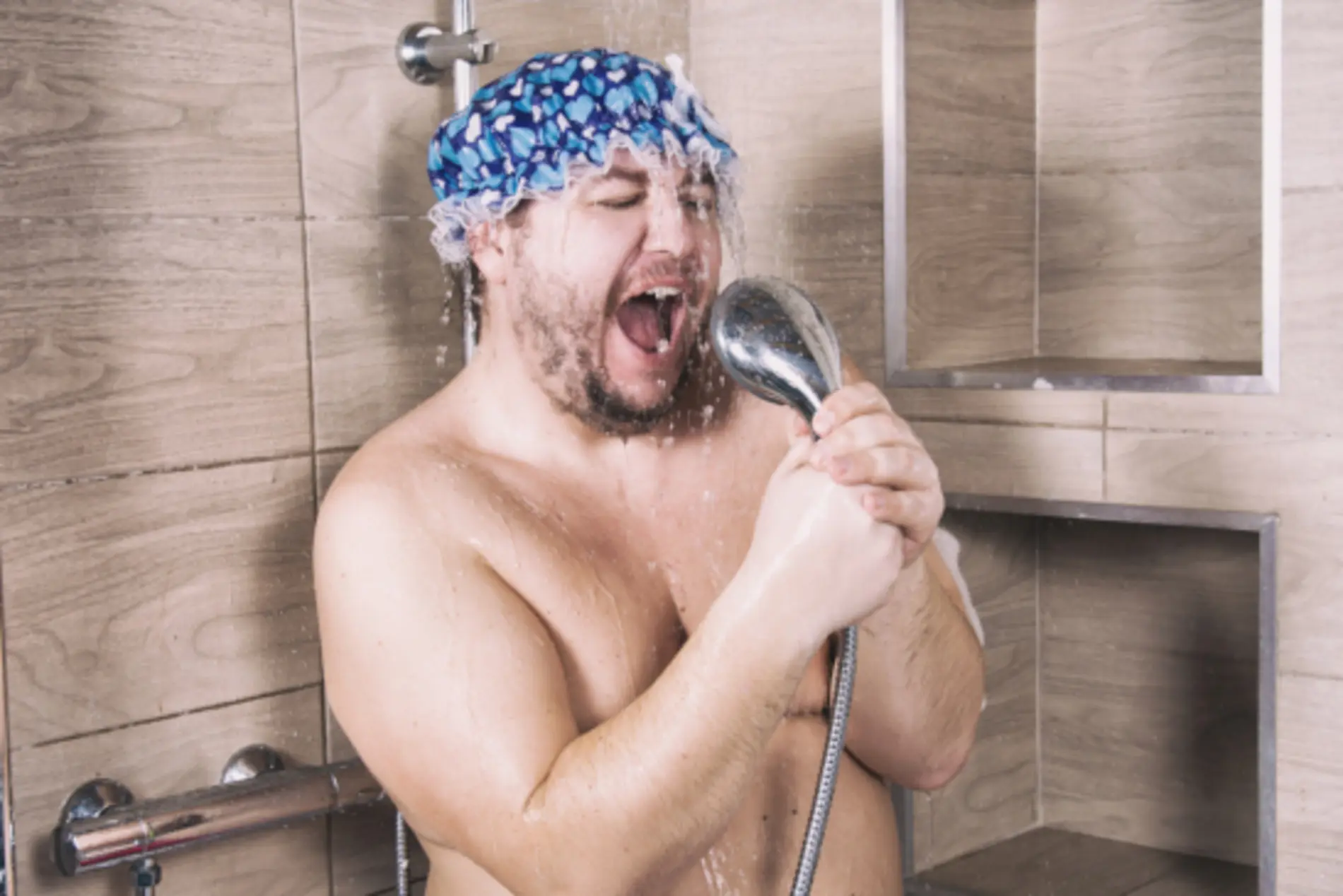 Ein Mann mit Duschhaube steht in der Dusche und singt emotional in den Duschkopf.