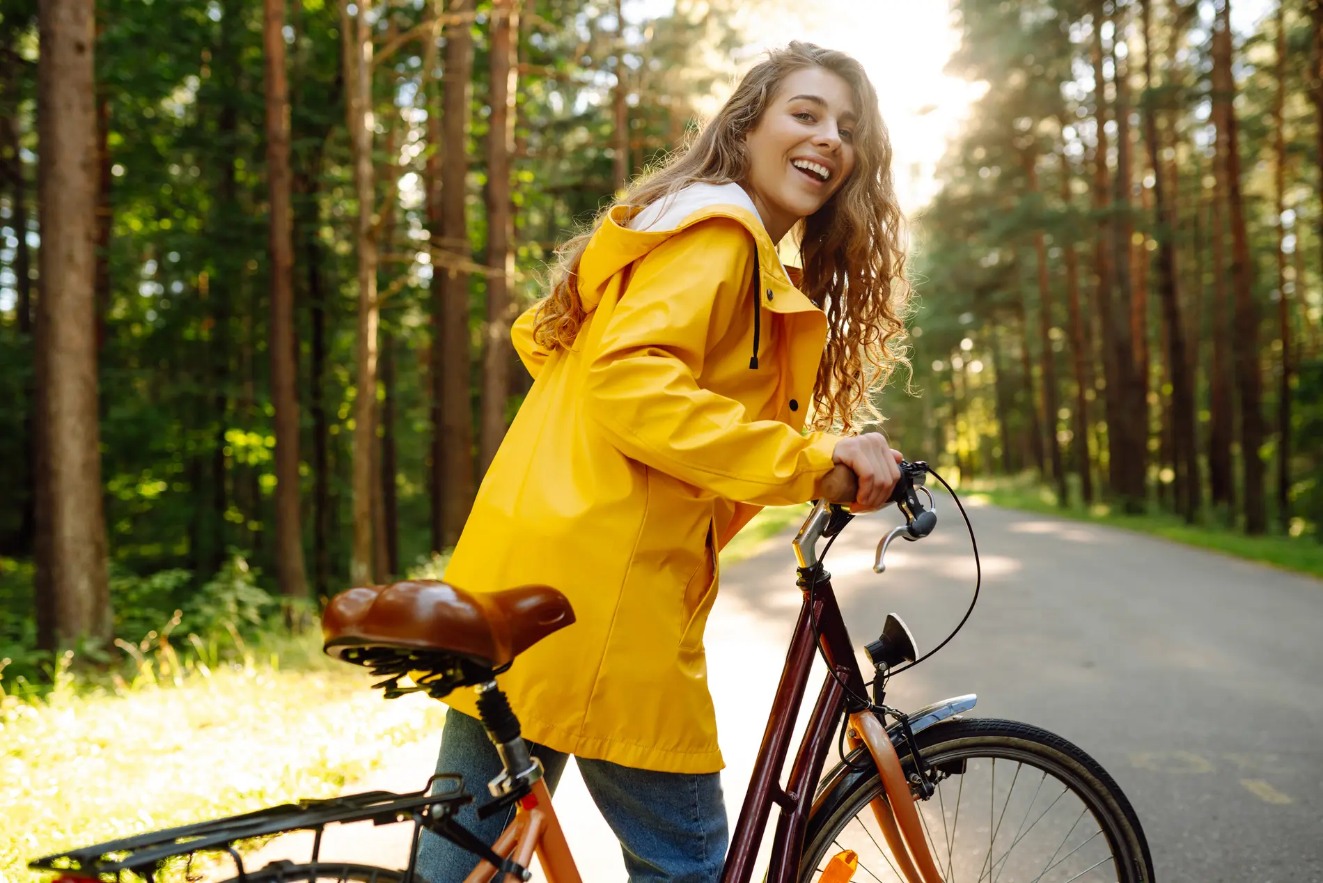 Frau mit gelber Jacke schiebt Fahrrad durch Waldgegend