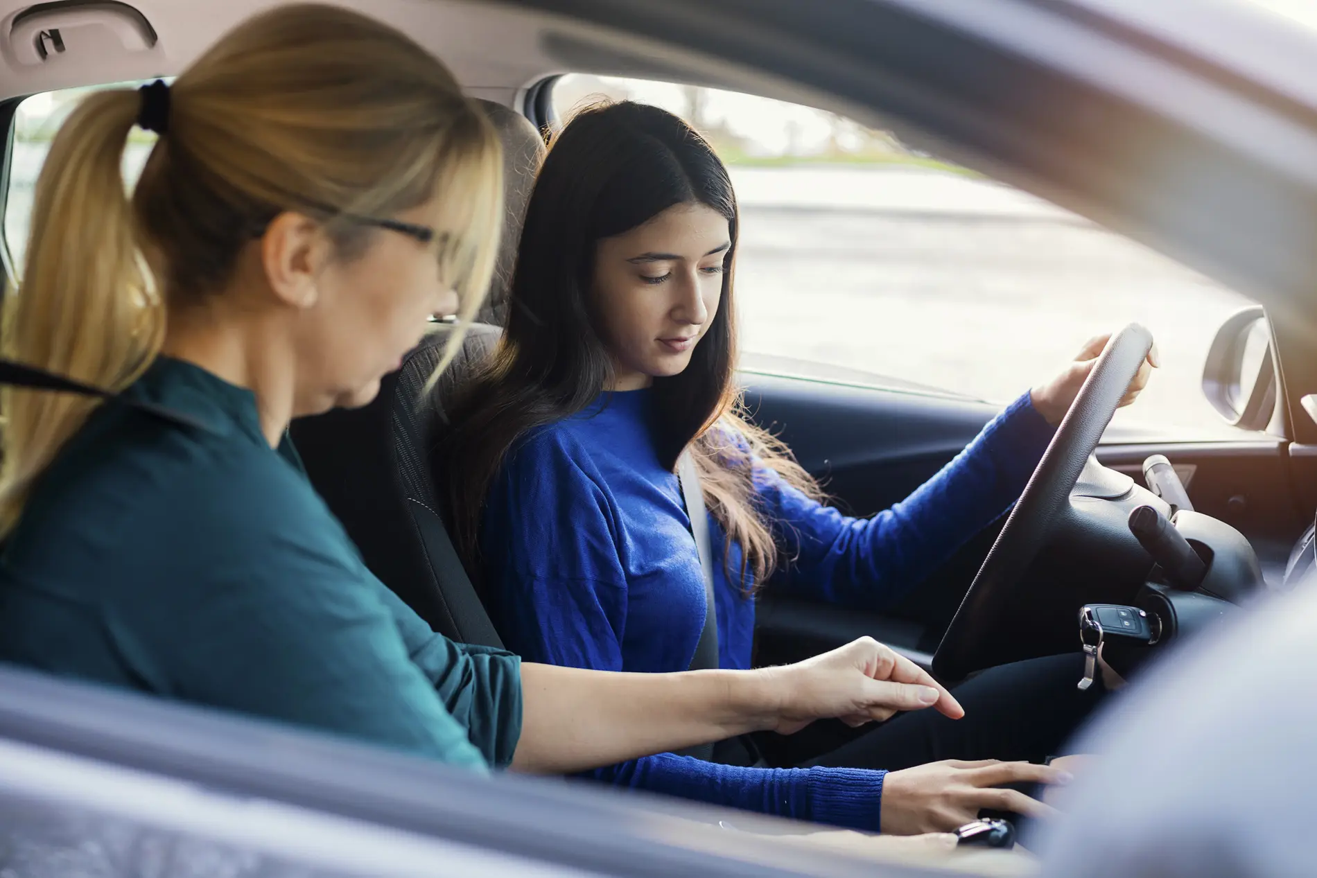 Fahrschülerin bekommt eine Einweisung ihrer Fahrlehrerin im Auto. Sie schauen auf die Gangschaltung.