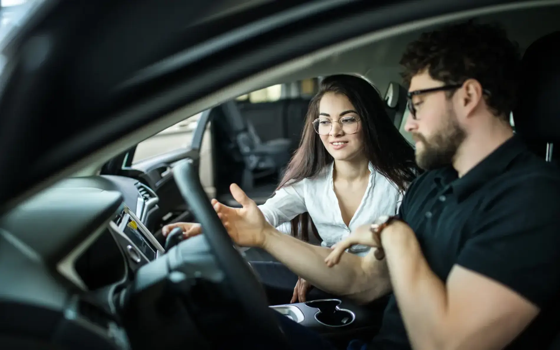 Fahrlehrerin und Fahrschüler sitzen im Auto. Sie erklärt den Boardcomputer.