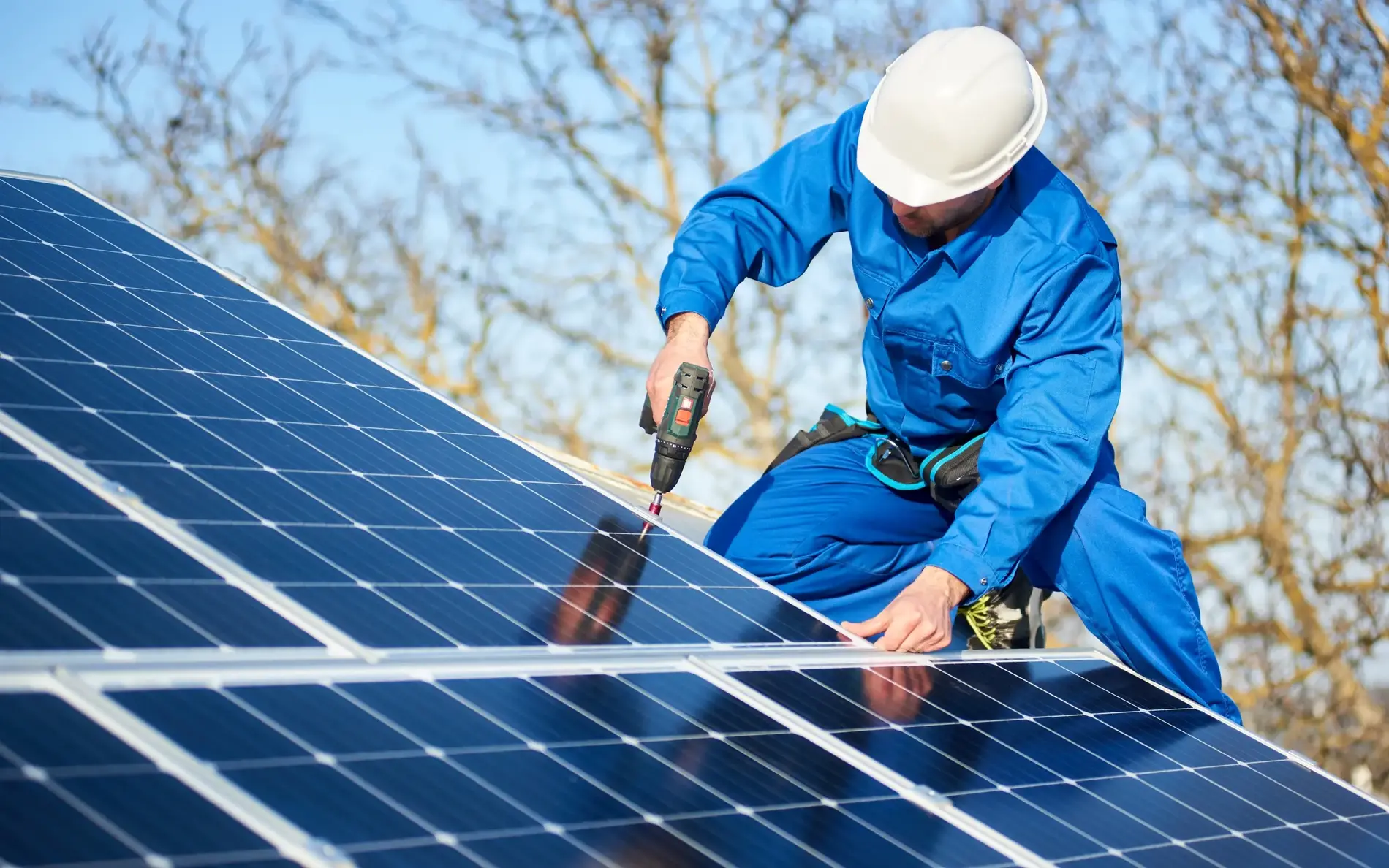 Ein Mann mit Helm und blauen Overall befestigt mit einem Akkuschrauber gerade die PV-Anlage