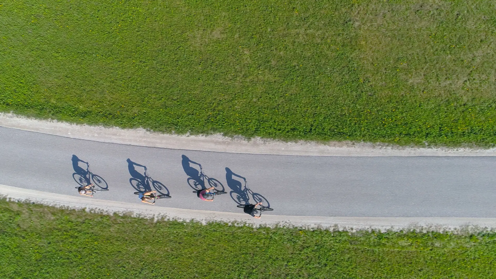 4 Radfahrer:innen von weit oben. Zu sehen sind die Schatten, die ihre Räder werfen.