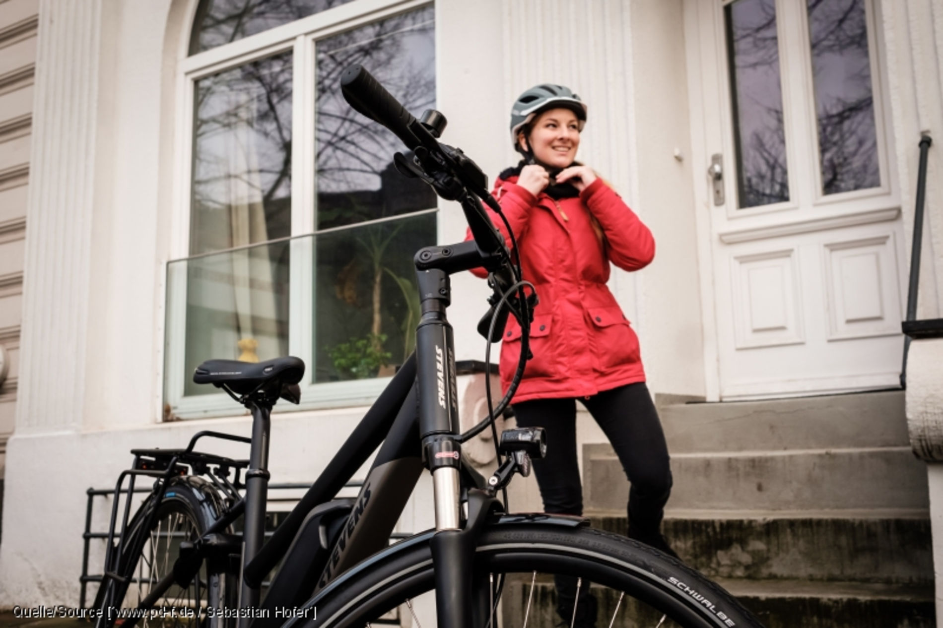 Eine junge Frau setzt sich gerade den Helm auf, vor ihr steht ein Fahrrad.